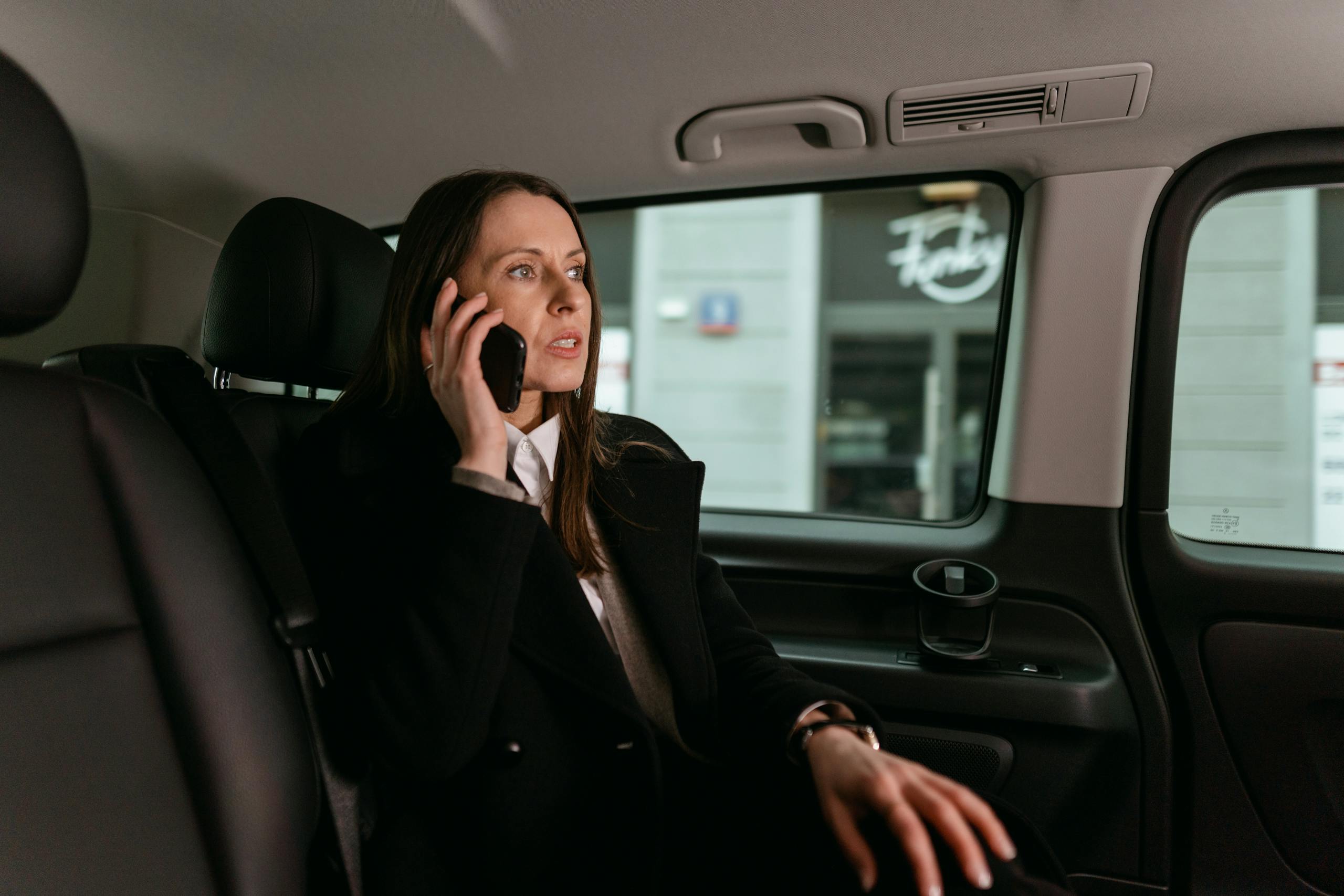 Confident businesswoman talking on phone inside a car. Professional attire, focused expression.